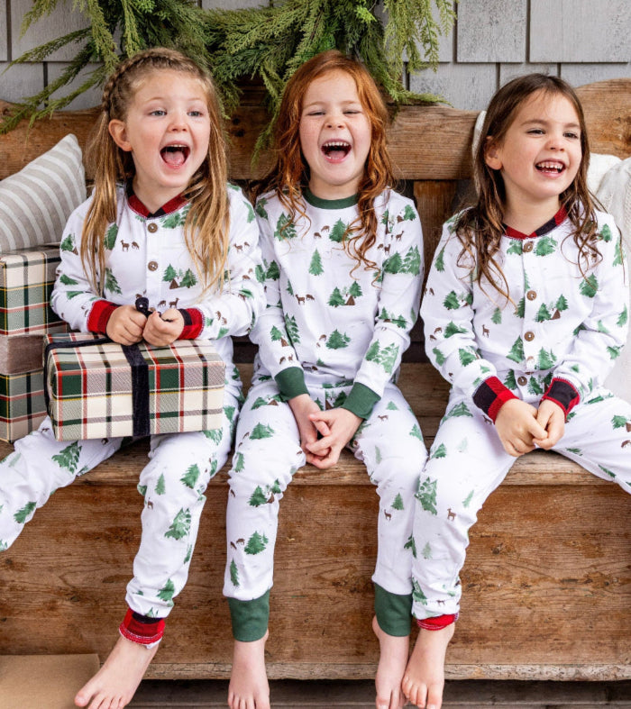 Three children in matching Christmas pajamas sitting on a wooden bench.
