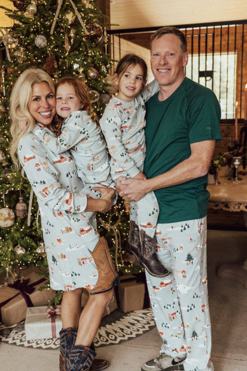 Family of four wearing matching pajamas in a festive living room with a Christmas tree.