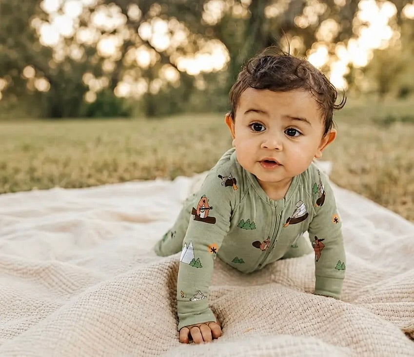 Baby in a green outfit with animal prints on a blanket outdoors