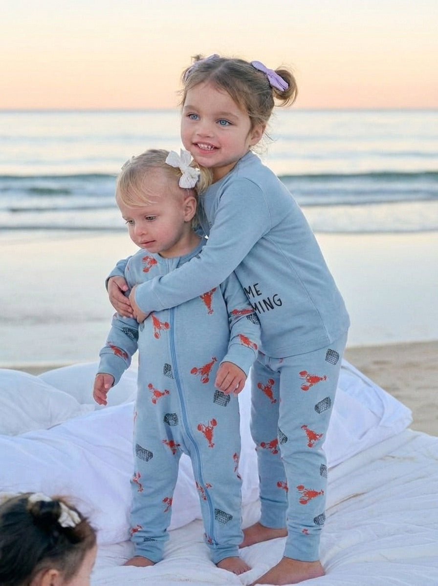 Two children in matching pajamas standing on a beach at sunset.