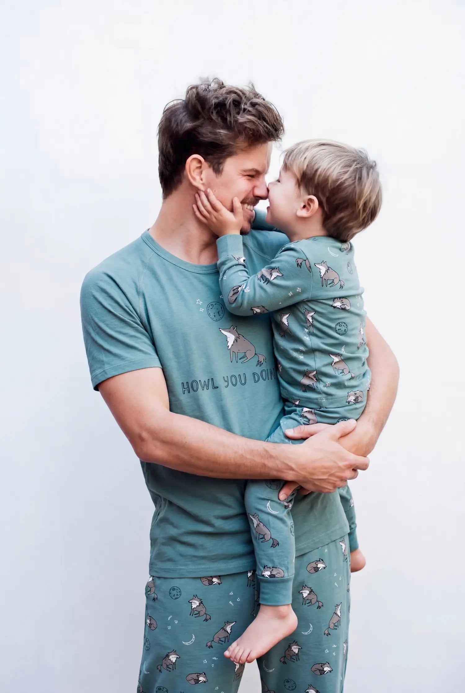 Man and child wearing matching teal pajamas with animal patterns against a white background