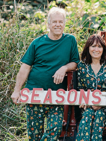 Family in matching pajamas with a 'Seasons Greetings' sign in front of a red truck with a Christmas tree.