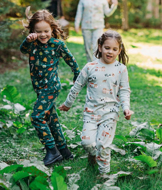 Three children in matching pajama sets running through a grassy outdoor area.