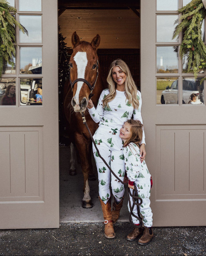Woman and child in matching outfits standing next to a horse in a stable.