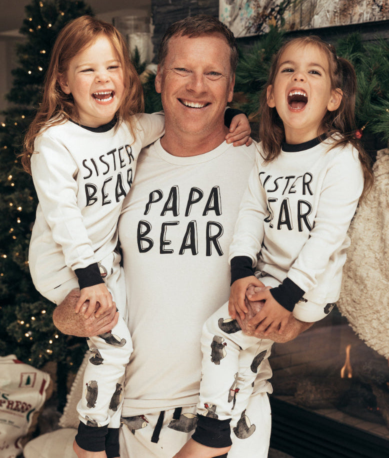 Man with two children wearing matching 'Papa Bear' and 'Sister Bear' pajamas in a festive setting.