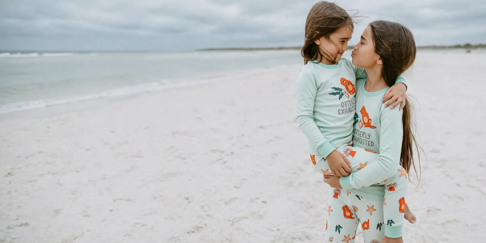 Two children in matching pajamas standing on a beach.