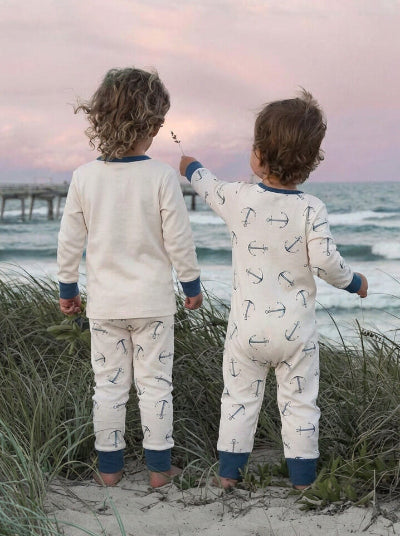 Two children in pajamas standing on a beach at sunset, facing the ocean.