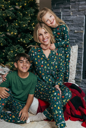 Woman and two children in matching green pajamas sitting in front of a Christmas tree.