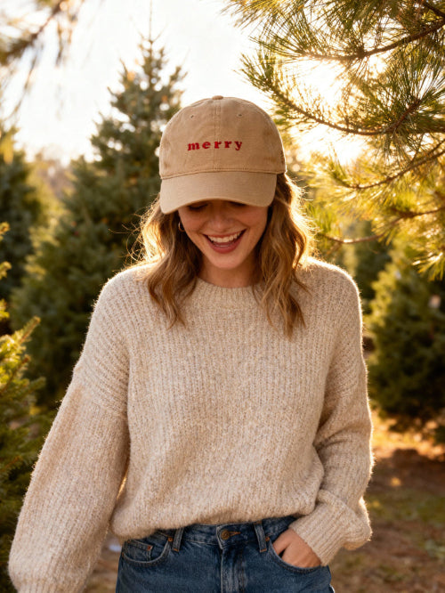 Person wearing a beige cap with 'merry' text, standing among trees.