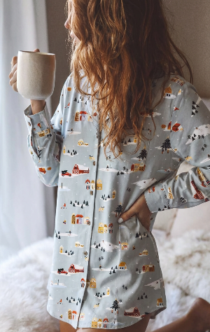 Person wearing a patterned pajama top holding a mug on a fluffy surface.