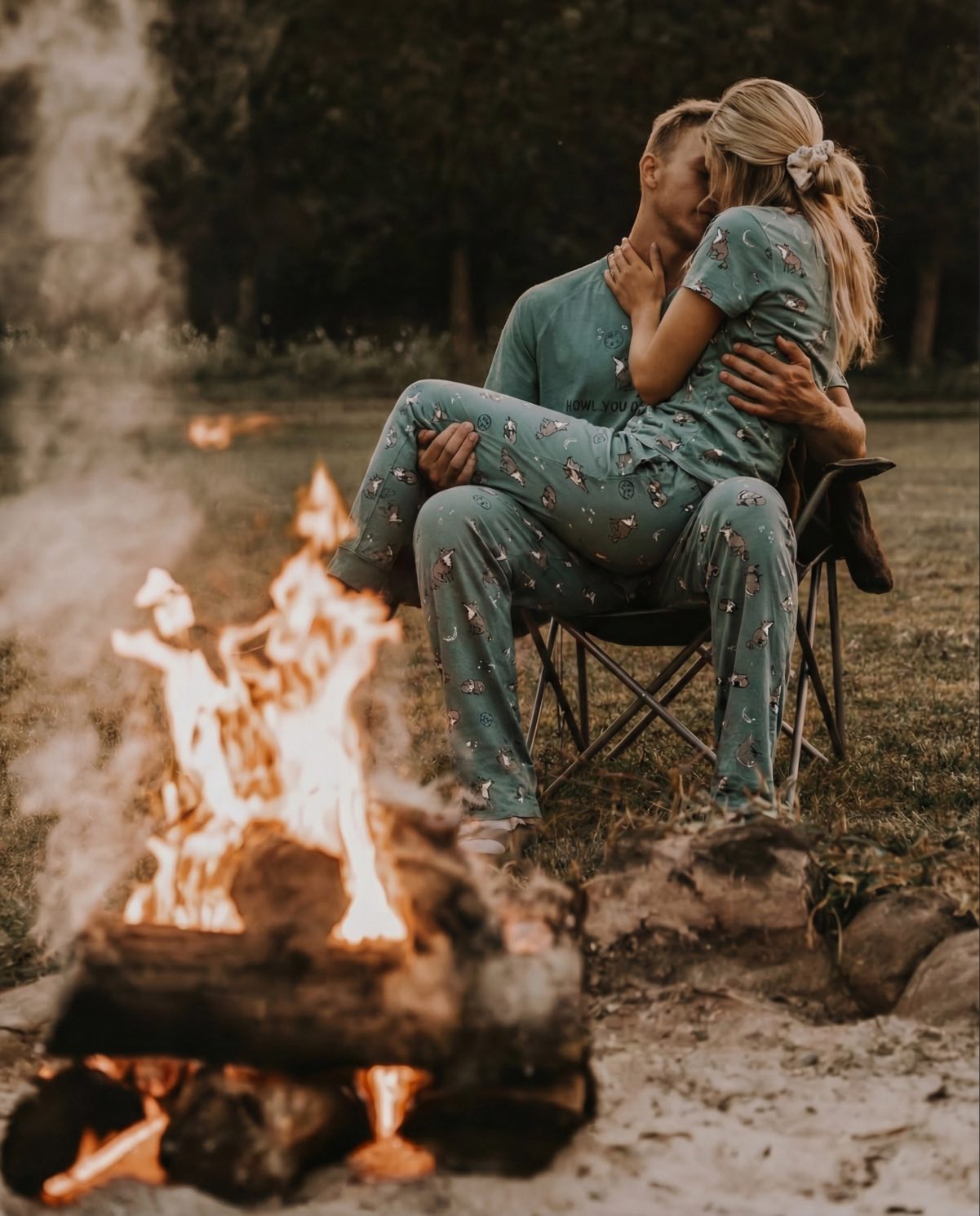 Couple in matching outfits sitting by a campfire in a natural setting